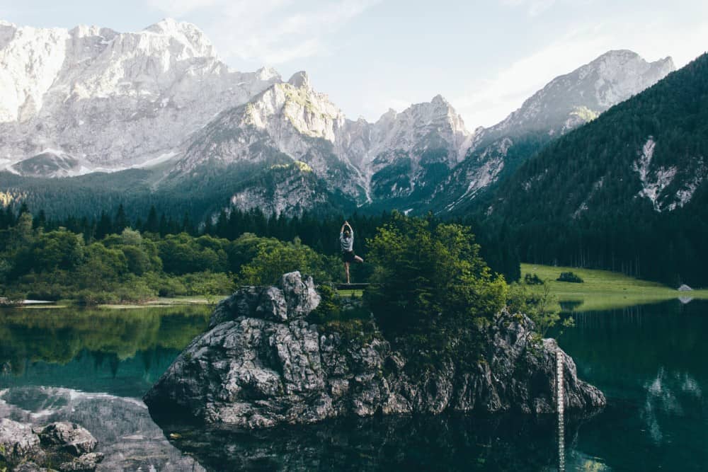 Eine Person steht auf einem Felsen in der Nähe eines Sees in den Bergen Österreichs.