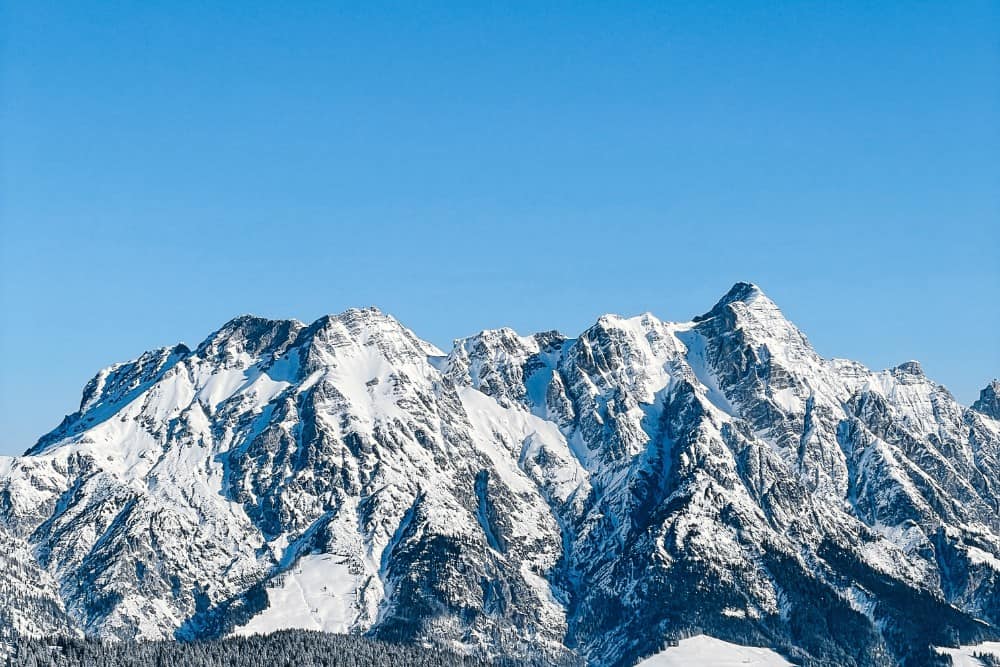 Das atemberaubende Saalbach-Gebirge in Österreich mit seinen majestätischen, mit makellosem weißem Schnee bedeckten Gipfeln sticht vor dem Hintergrund eines klaren blauen Himmels hervor.